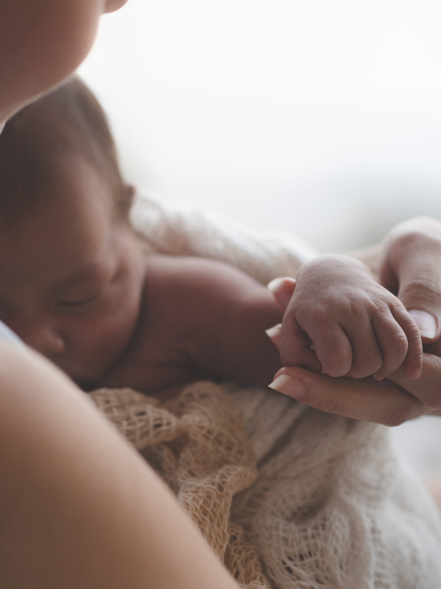 Close up of mum holding hand of newborn baby