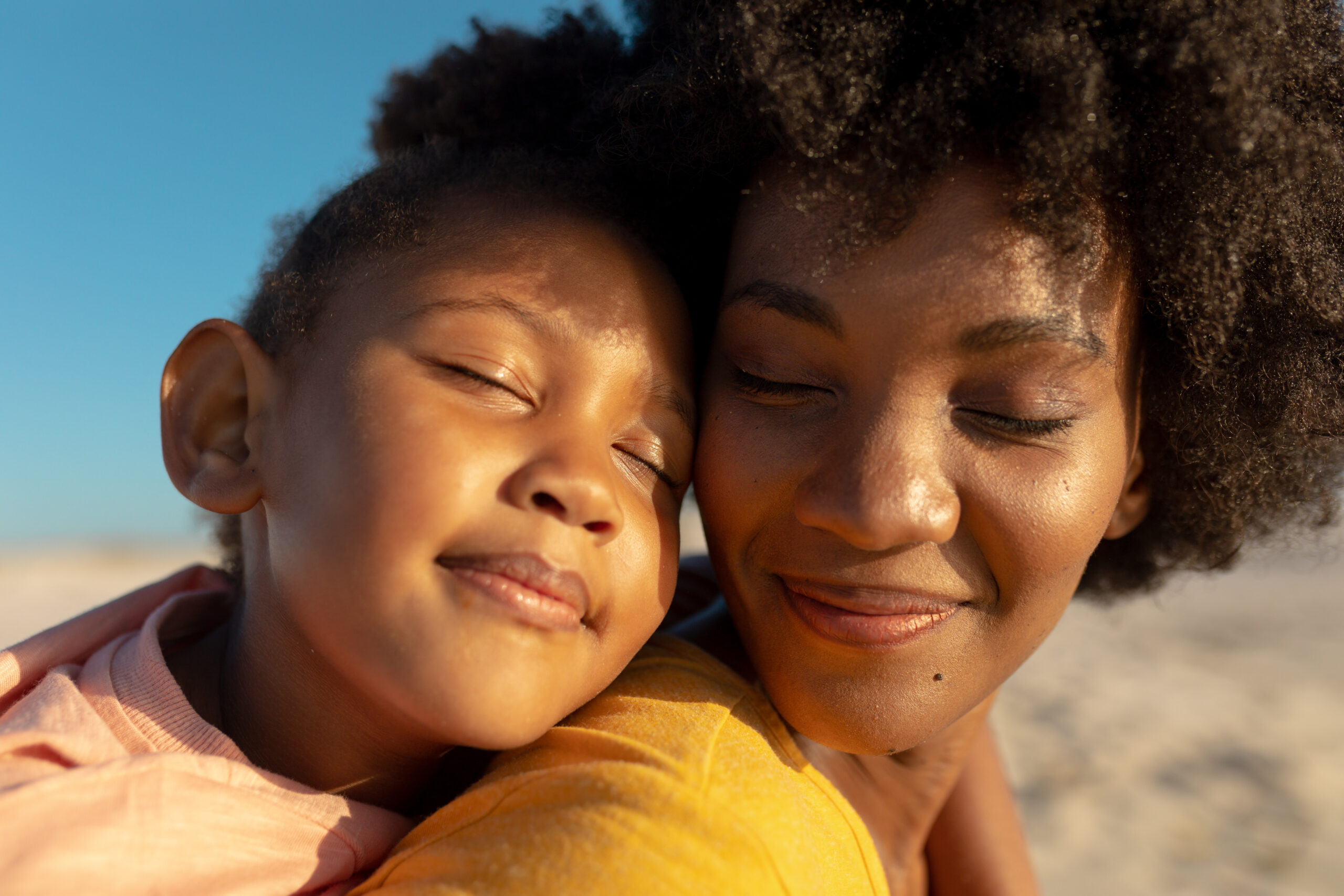 Close-up of girl with eyes closed relaxing on mother's shoulder at beach