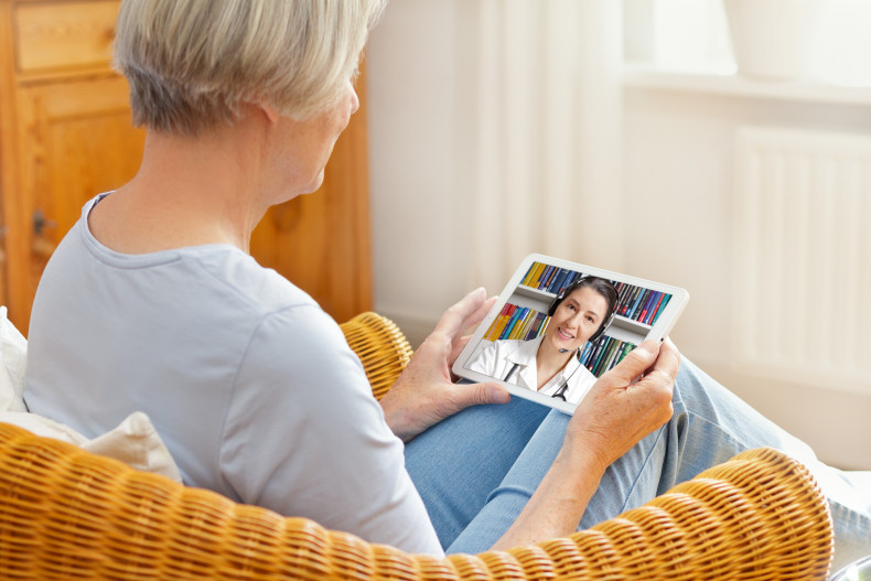 A woman sitting in an armchair using a tablet to take part in a remote appointment