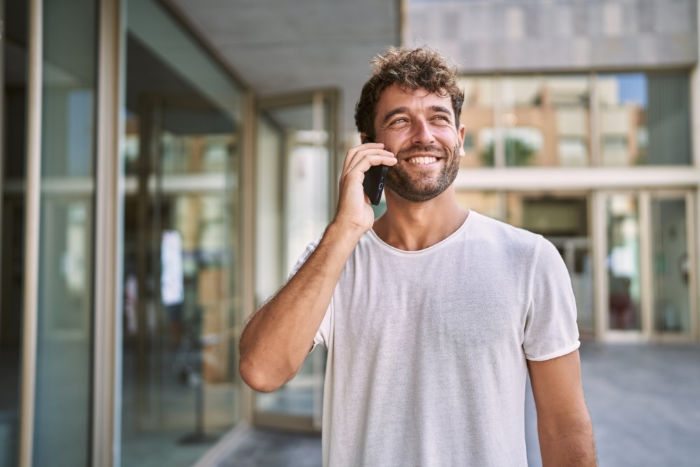 Young man walking in the street smiling and confidently talking on the phone.