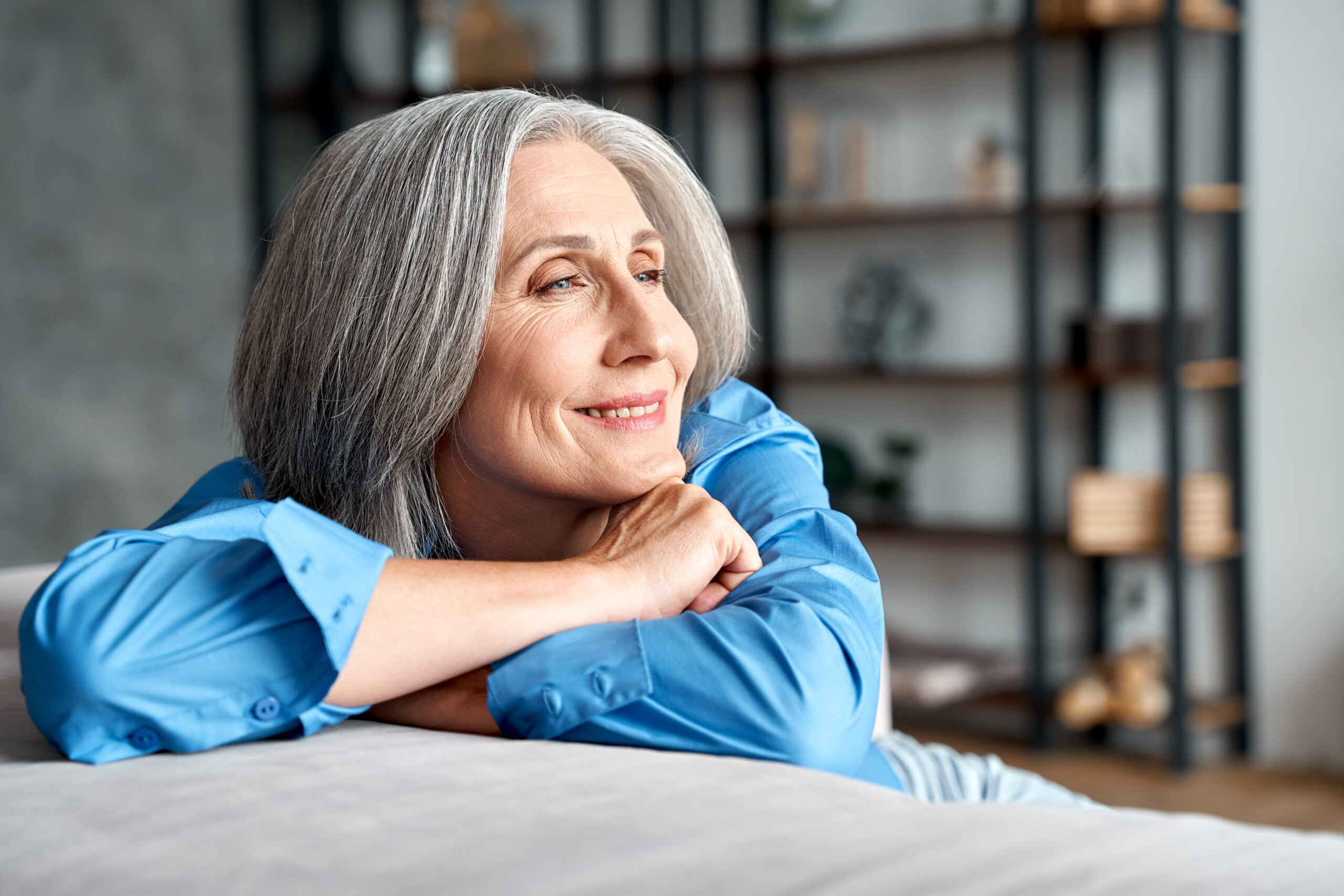 Happy relaxed mature old woman resting dreaming sitting on couch at home.