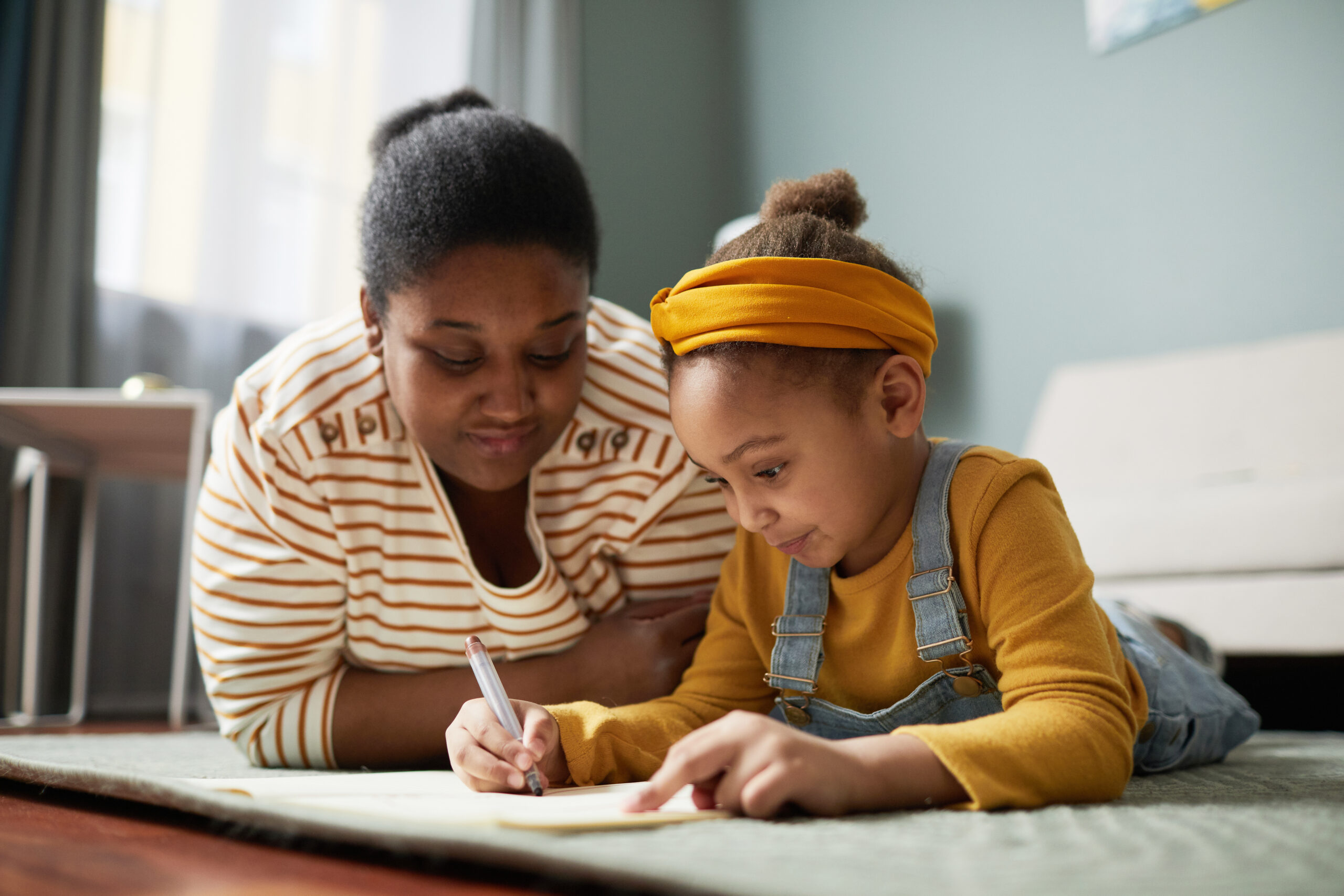 Girl drawing on floor with mother in cozy home interior