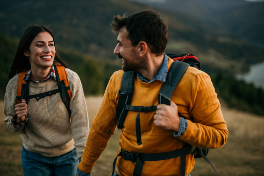 An image of a loving couple, wearing their camping backpacks as they wind down from a day of adventure