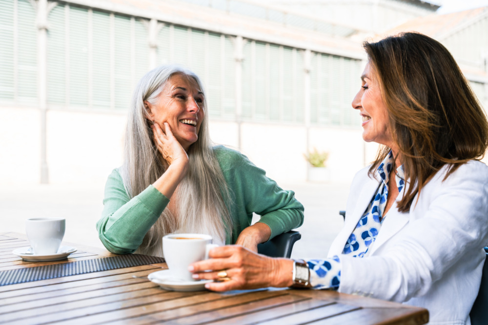 Two senior women talking and laughing over a coffee in a bright cafe