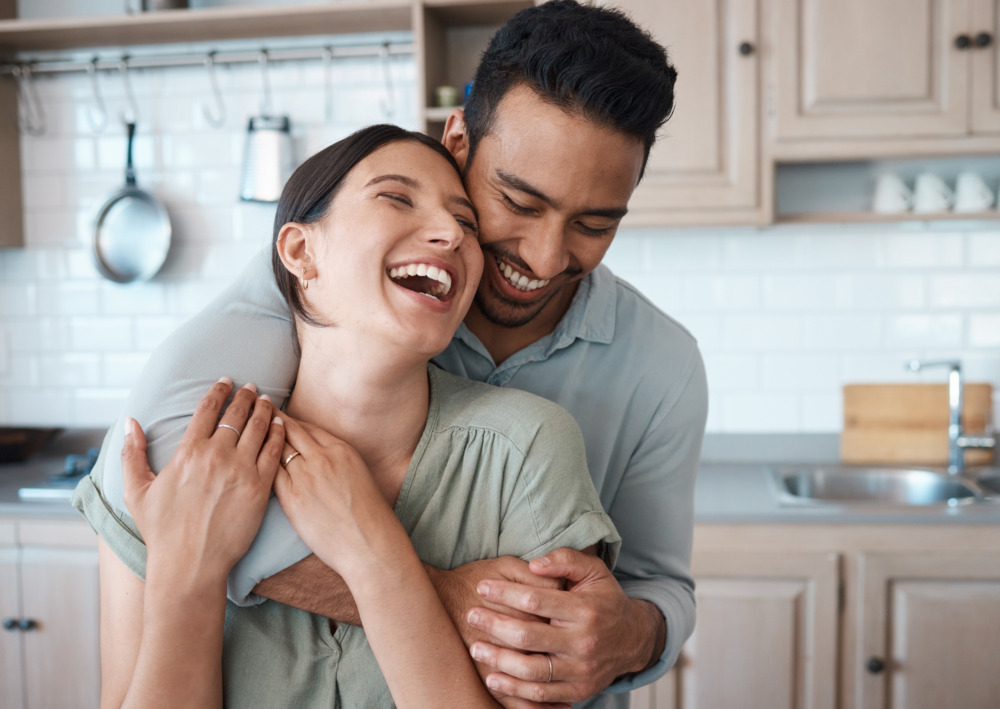 A young couple embracing and laughing together in their kitchen.