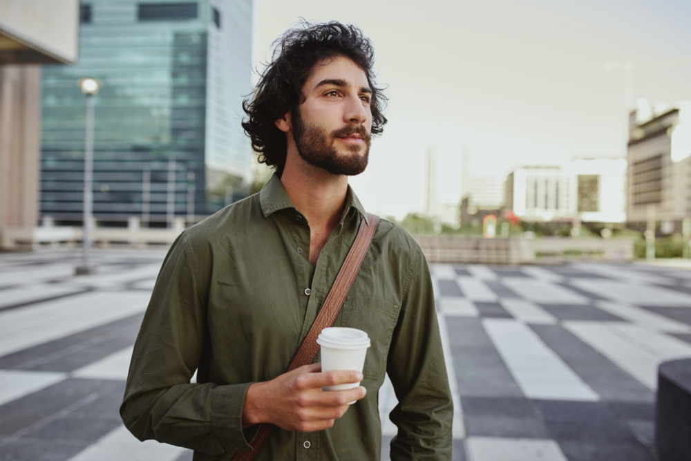 Man holding takeaway coffee cup standing outside and looking away.