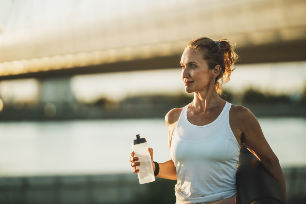 Woman out for a run next to a river, holding a water bottle.