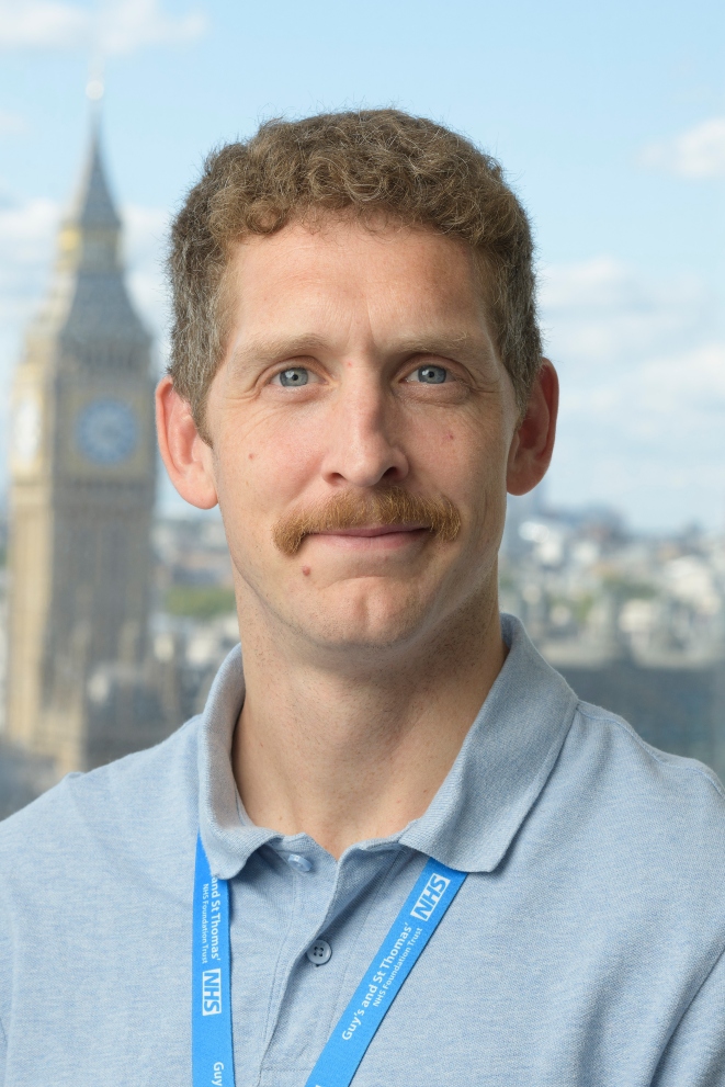 Man with curly hair and moustache smiling for professional headshot