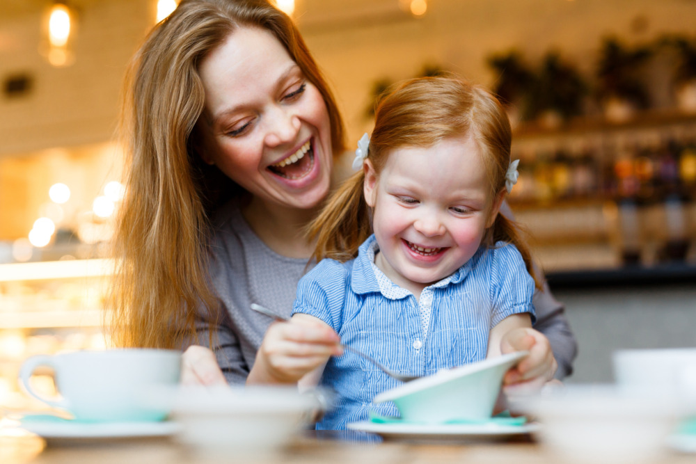 Cheerful woman and her young daughter eating in a cafe