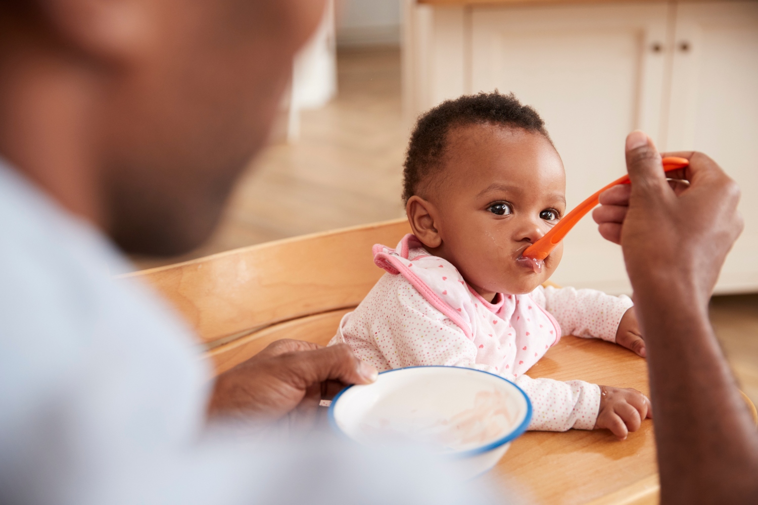 Father spoon feeding his baby daughter in high chair