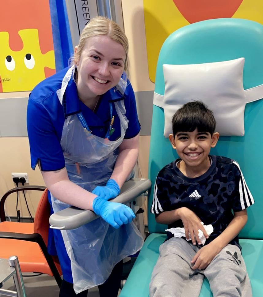 Smiling boy in hospital bed next to smiling blonde nurse