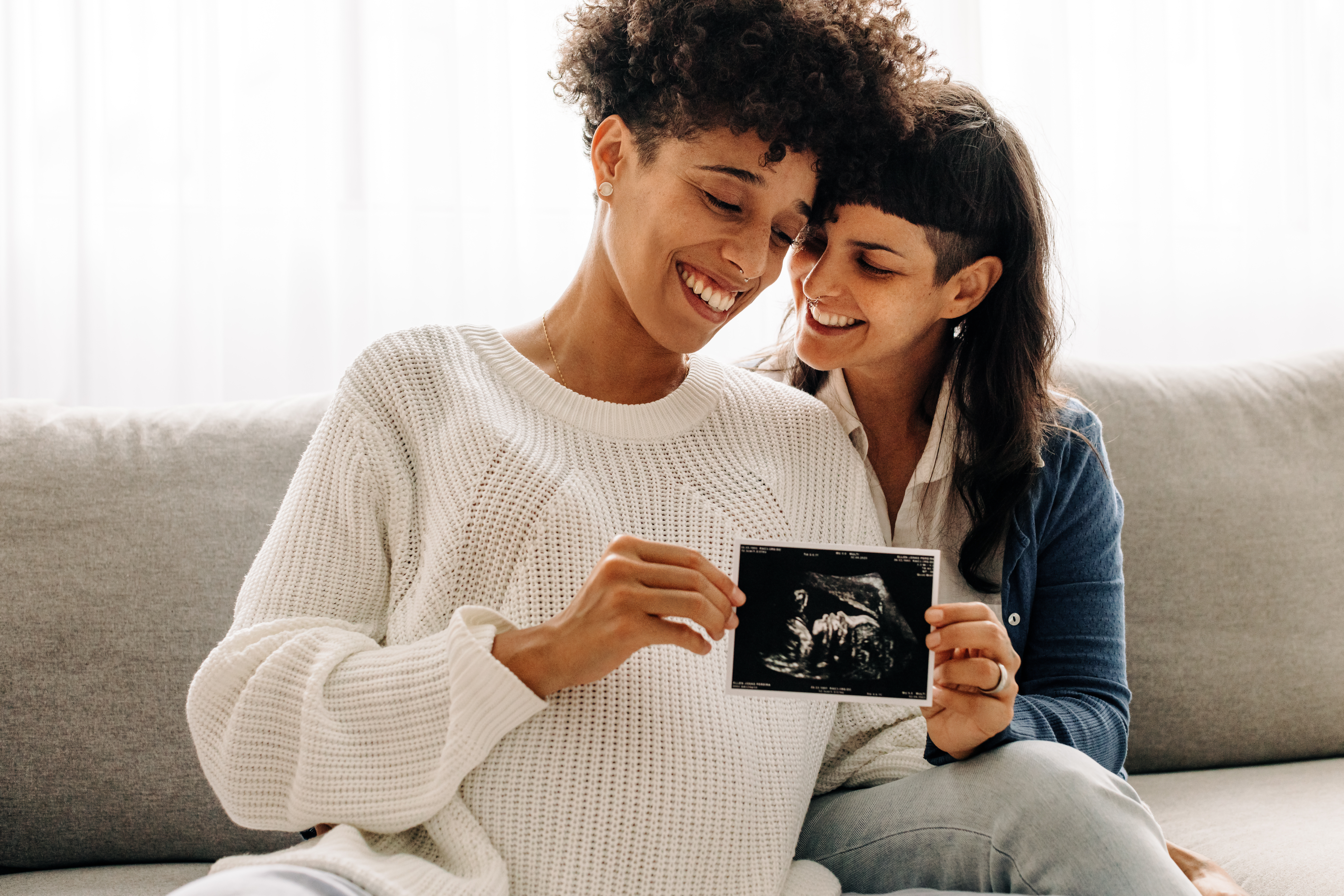 Same-sex pregnant couple holding up their ultrasound scan.