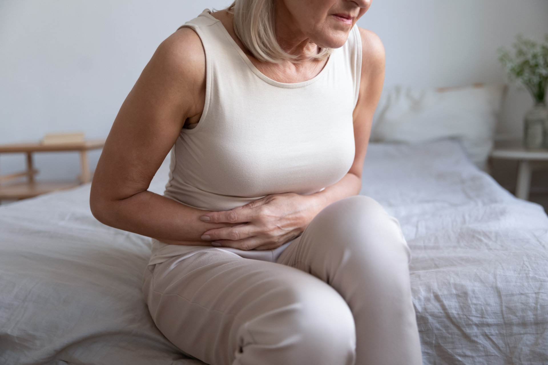 Older woman embracing belly, suffering from strong stomach ache. Feeling discomfort in abdomen suspected pancreatitis, gastritis or diarrhoea.