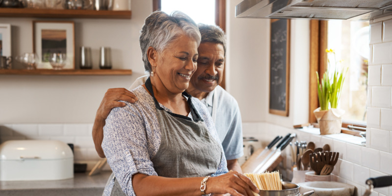Older couple cooking together in the kitchen, in an embrace.