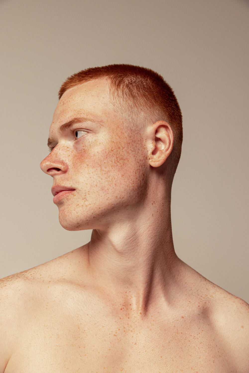 Close up image of a young man looking off to the side against a neutral studio background