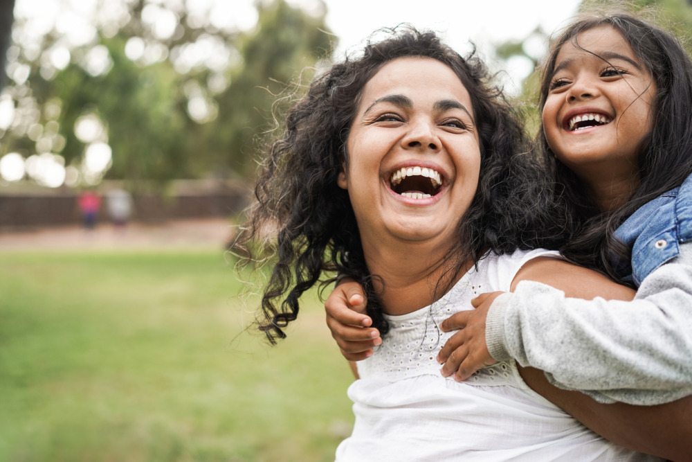 Happy laughing mother giving her daughter a piggy back in a field.