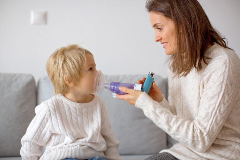 Mother, helping little toddler child with inhaler with spacer, at home